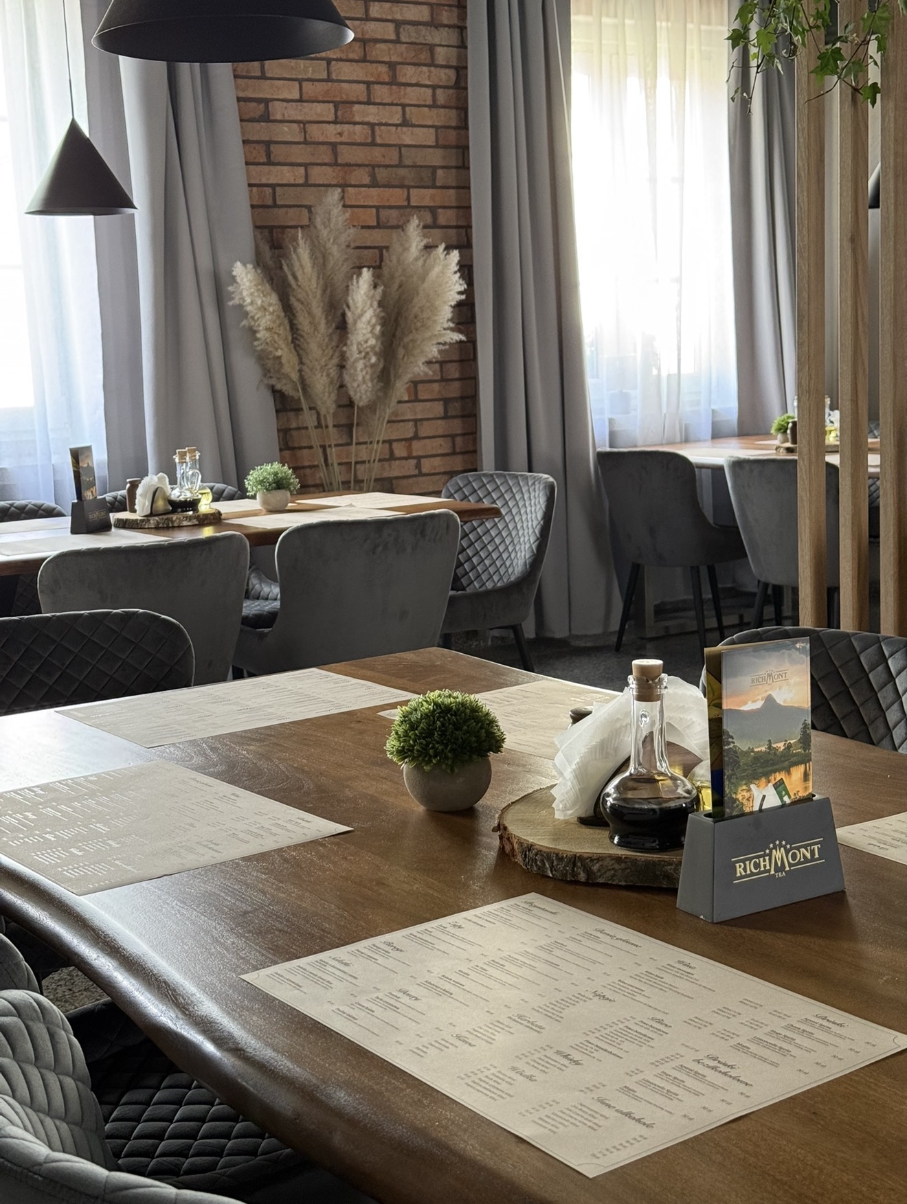 Wnętrze restauracji z ceglaną ścianą, drewnianymi stołami i szarymi fotelami